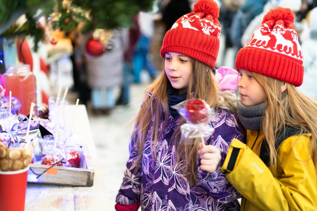 Two children in winter clothes choose homemade sweets at the Christmas market.